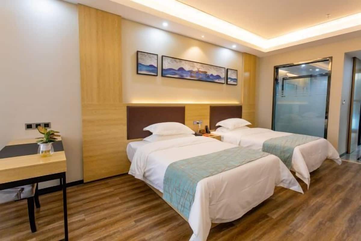 A hotel room with two beds, a desk, and a wall-mounted artwork.