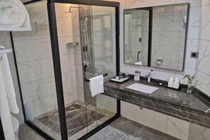 Un baño moderno con ducha envuelta en vidrio, un espejo grande y encimera de mármol.