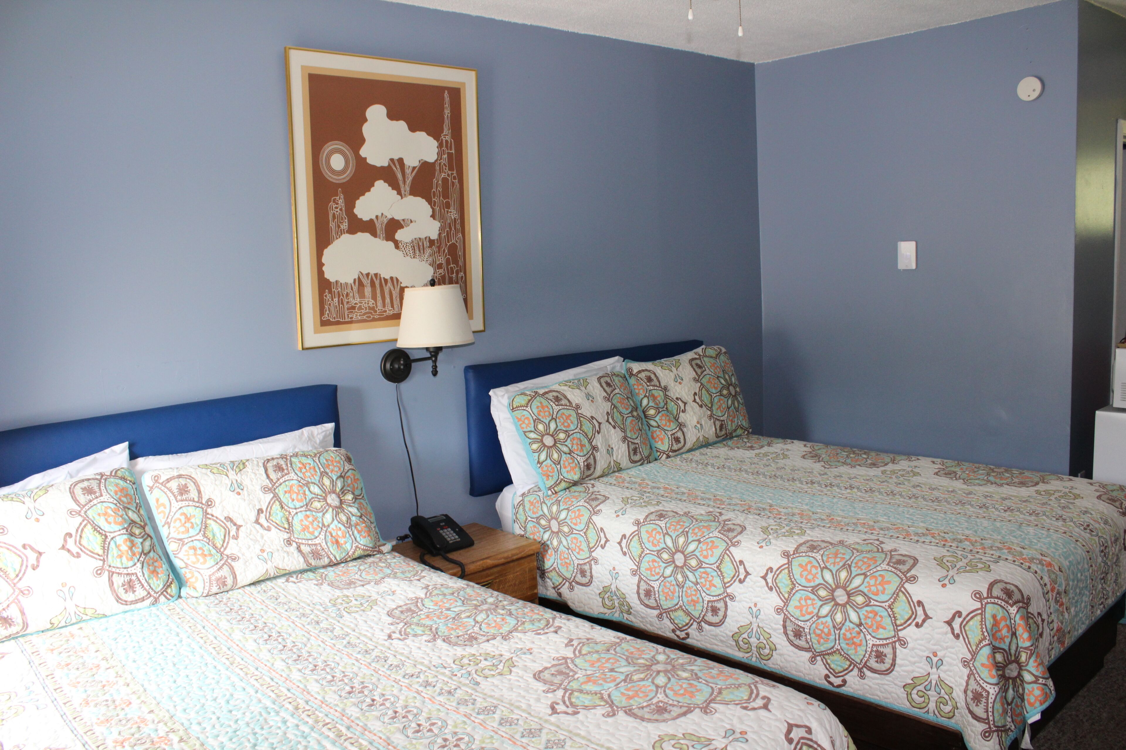 A bedroom with two beds, a nightstand, a lamp, and a framed picture on the wall.