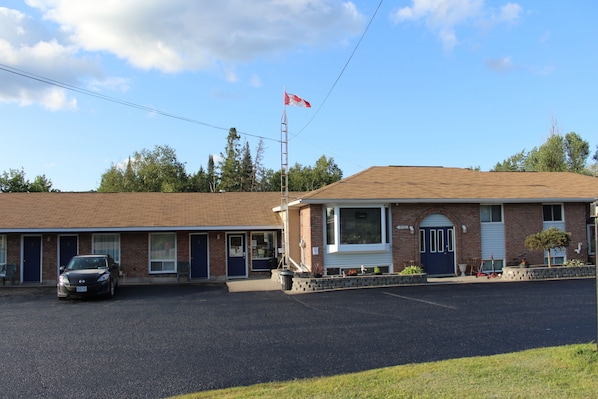 A motel with a parking lot, a flagpole with a flag, and a car parked in front.