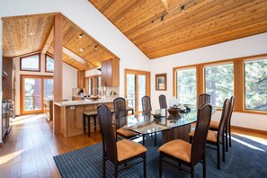 A spacious kitchen with wooden beams, a central island, and large windows offering a view of trees. - Creekside Lodge on GC w/ AC & Pool Table (Truckee)
