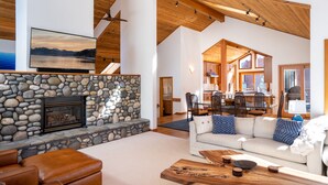 A spacious living room with a stone fireplace, a large flat-screen TV, leather seating, and a wooden coffee table. - Creekside Lodge on GC w/ AC & Pool Table (Truckee)