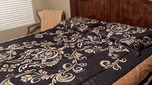 Ein Bett mit dunkelbrauner Kopfteil und einer Bettdecke in Schwarz und Beige.