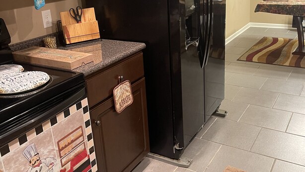 Eine Küche mit einem schwarzen Kühlschrank, einer Mikrowelle und einem Herd. Auf der Arbeitsplatte liegen ein Schneidebrett und eine Schere.