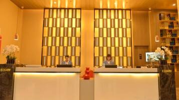 A reception desk with two receptionists, a check-in counter, and a wall with a geometric pattern.