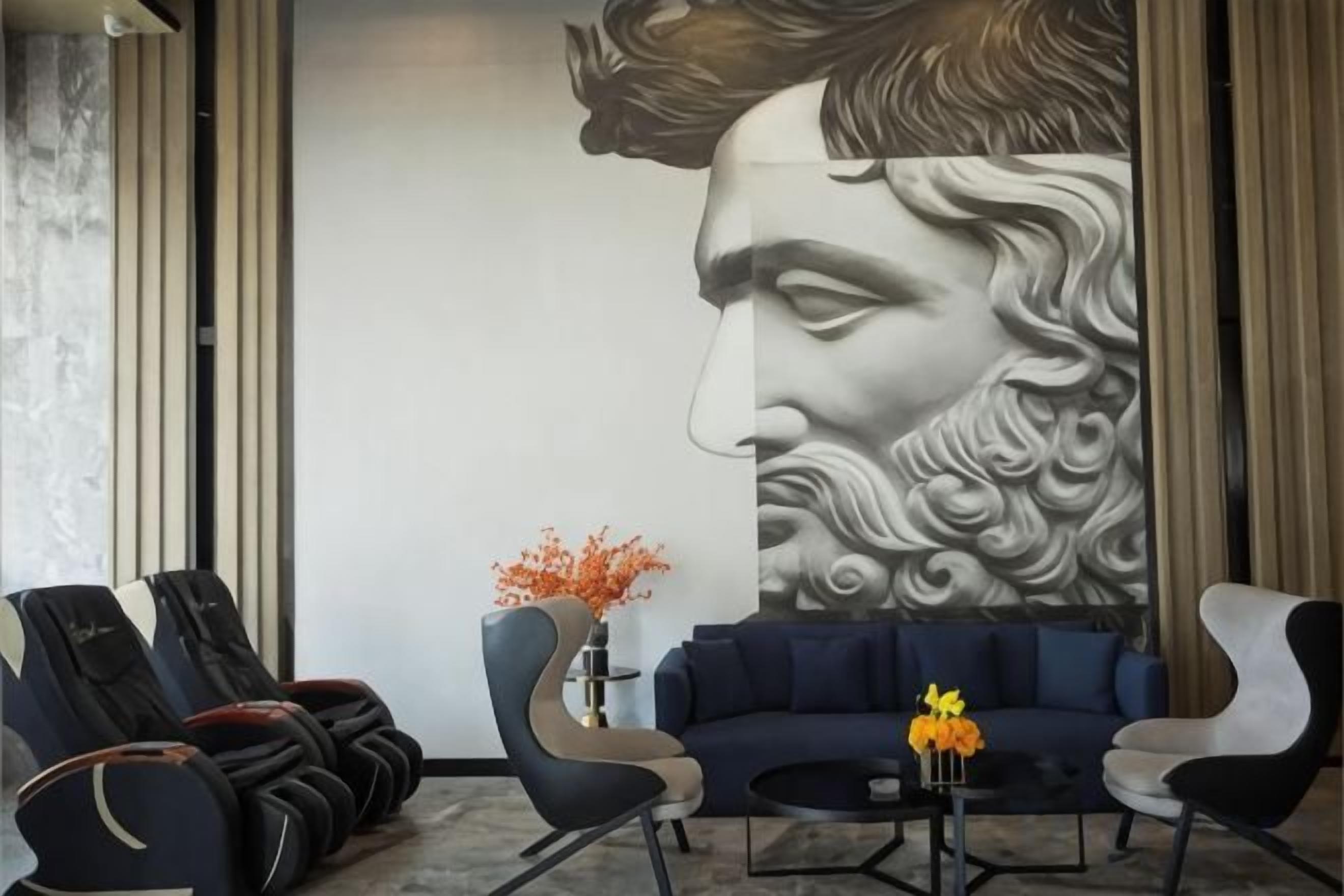 A lobby with a large mural, seating area, massage chairs, and a vase with flowers.