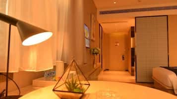 A hotel room with a bed, a bedside lamp, a small plant, and a view of the hallway.