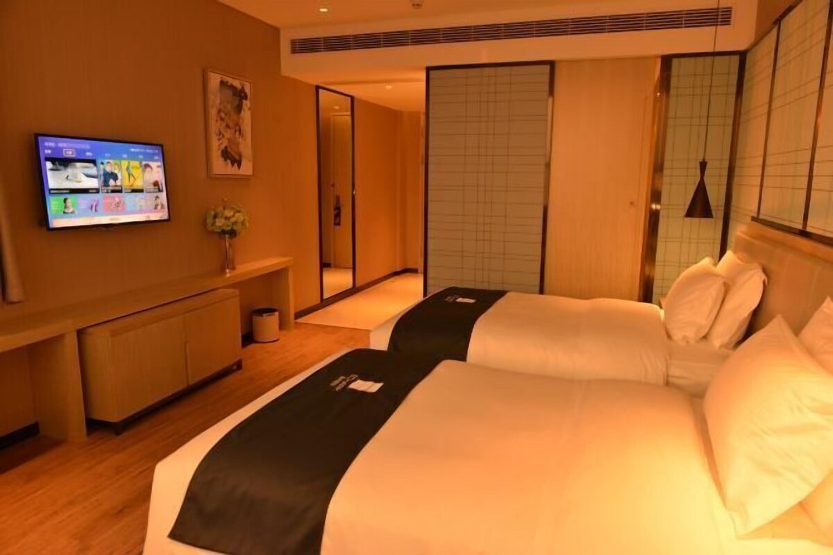 A hotel room with a bed, a TV, a mirror, and a sliding door.