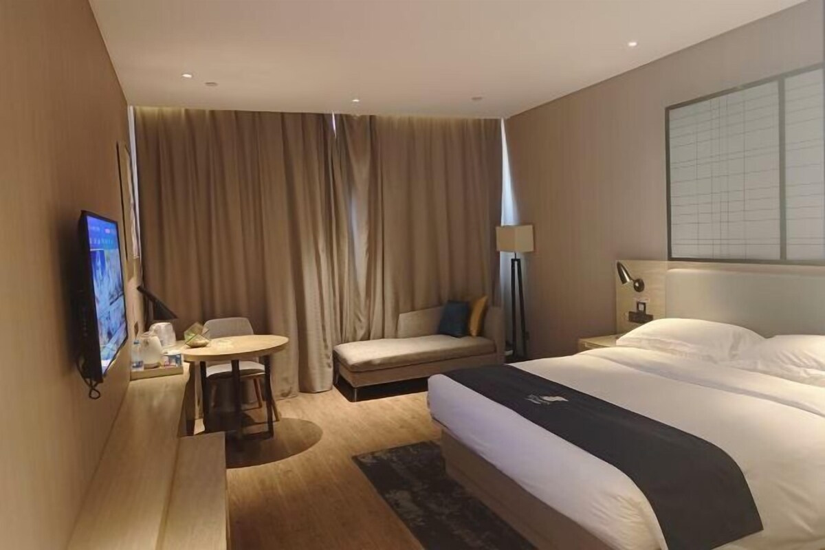 A hotel room with a bed, a sofa, a small table, a TV, and a window with curtains.