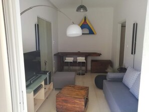 A modern living room with a TV, wooden coffee table, sofa, and a dining area with chairs and a table.
