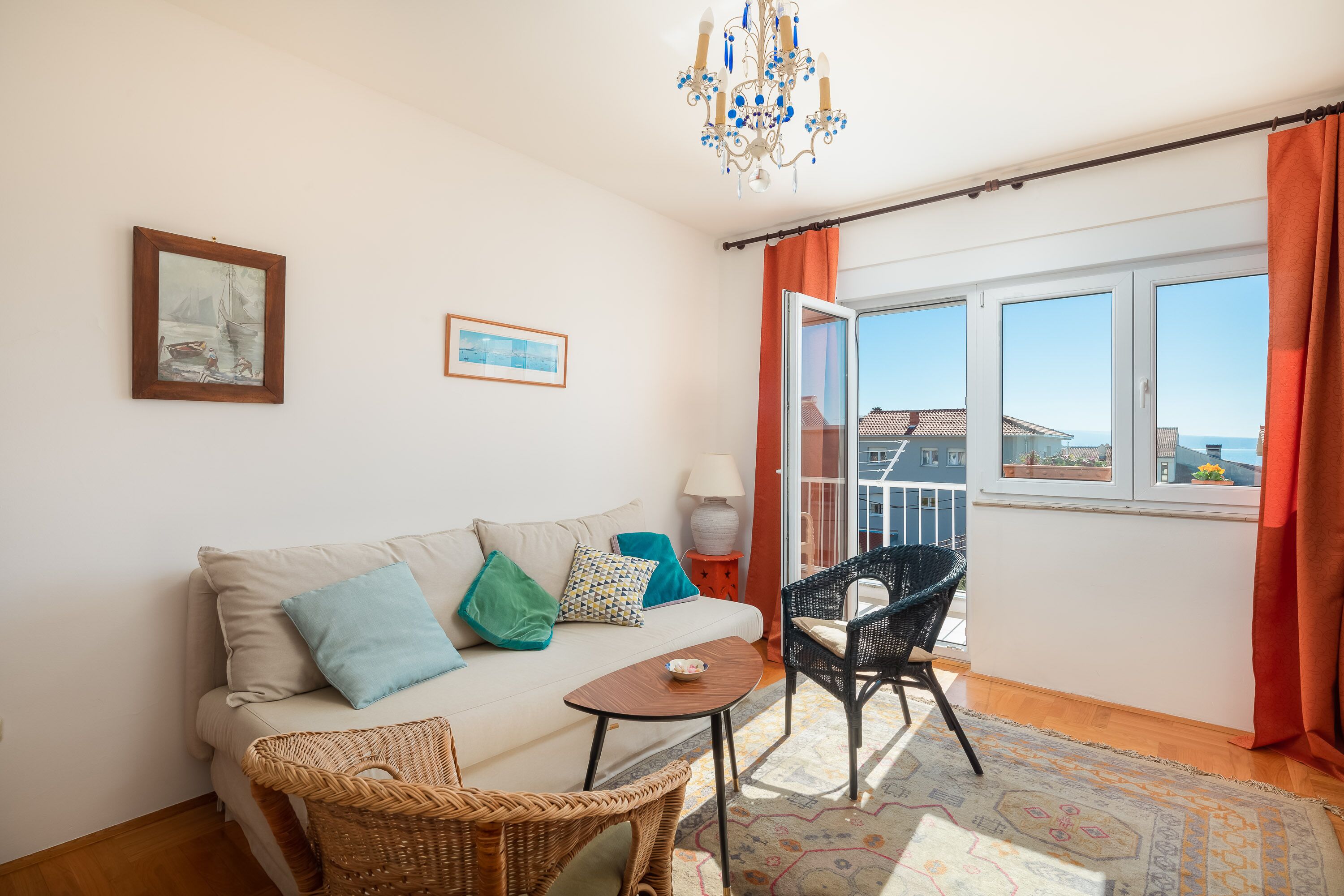 Una sala de estar acogedora con un sofá, una mesita, un sillón de mimbre y vistas al exterior desde una puerta abierta.