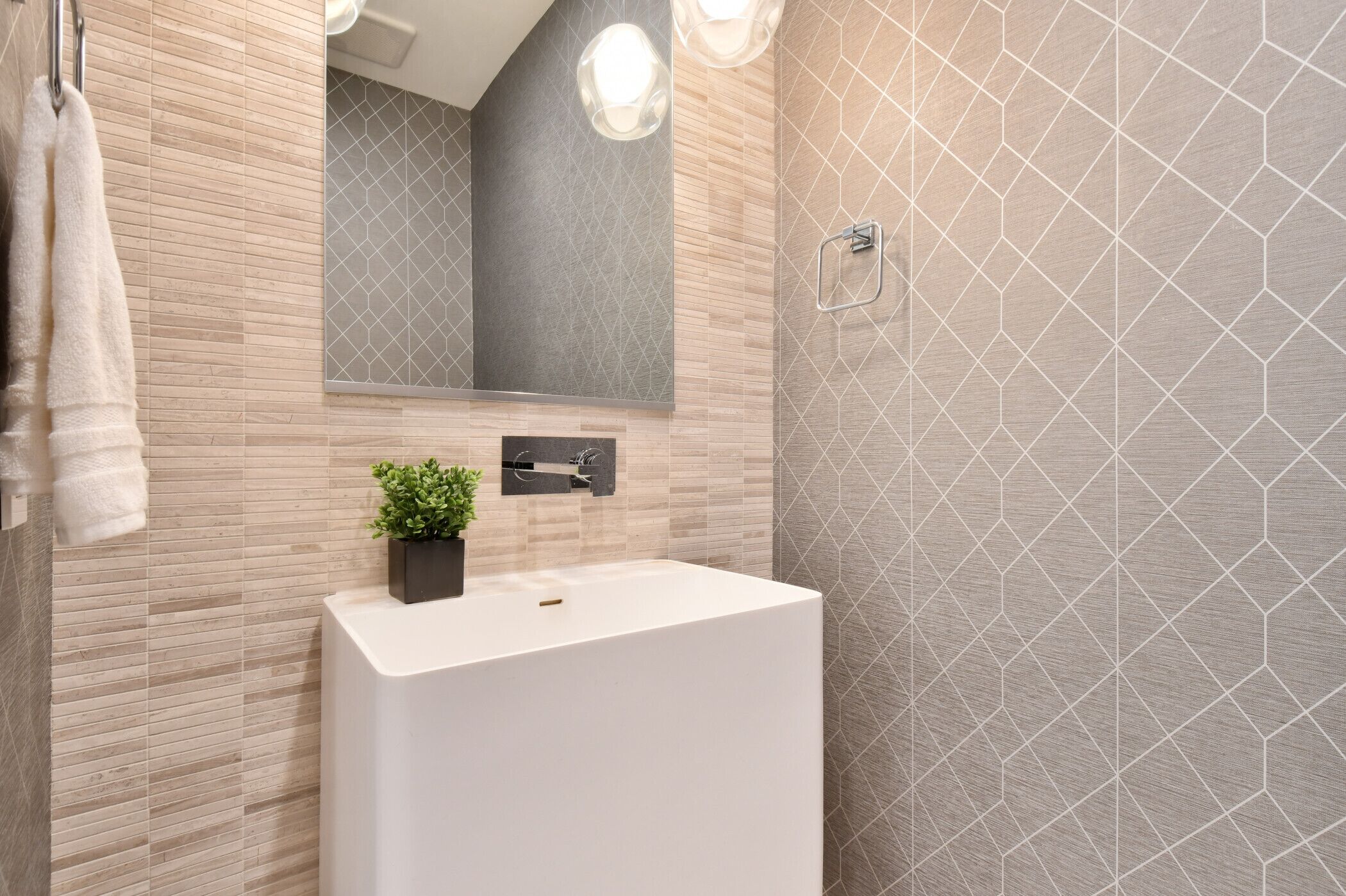Een moderne badkamer met een grote spiegel, een witte wastafel en een wand met een geometrisch patroon.