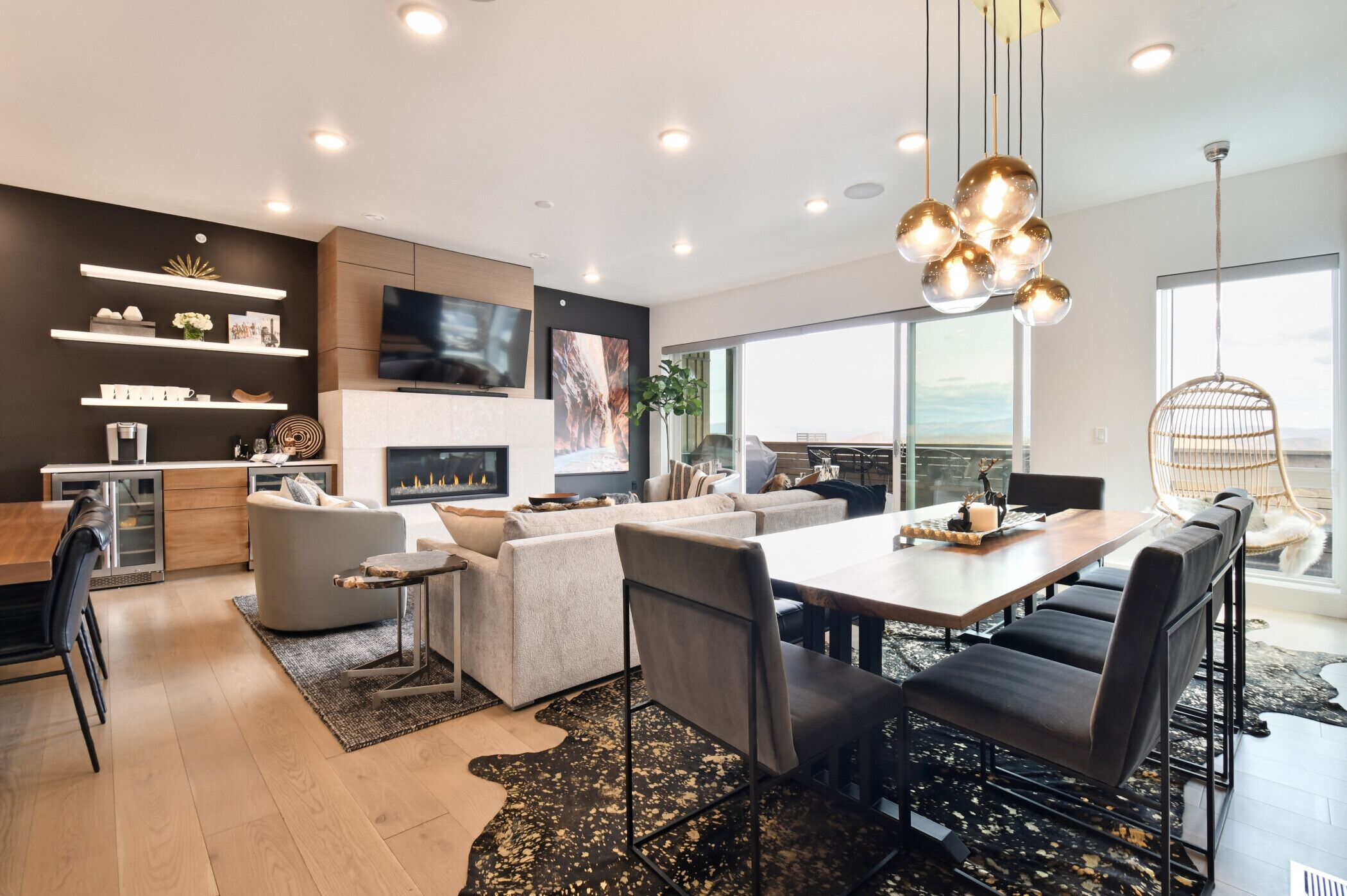 A modern living room with a fireplace, a dining area, and a large window offering a view.