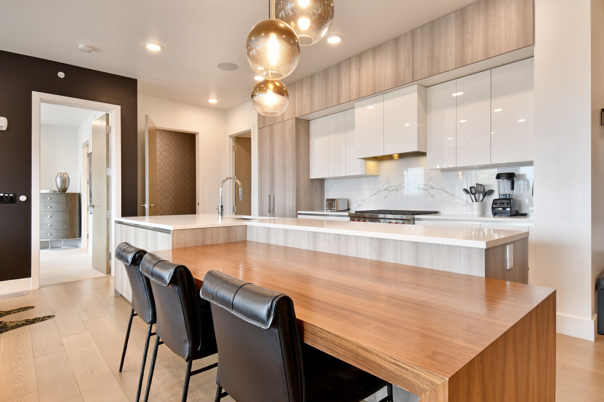 Una cocina moderna con una isla grande, sillas negras y una mesa de comedor de madera.