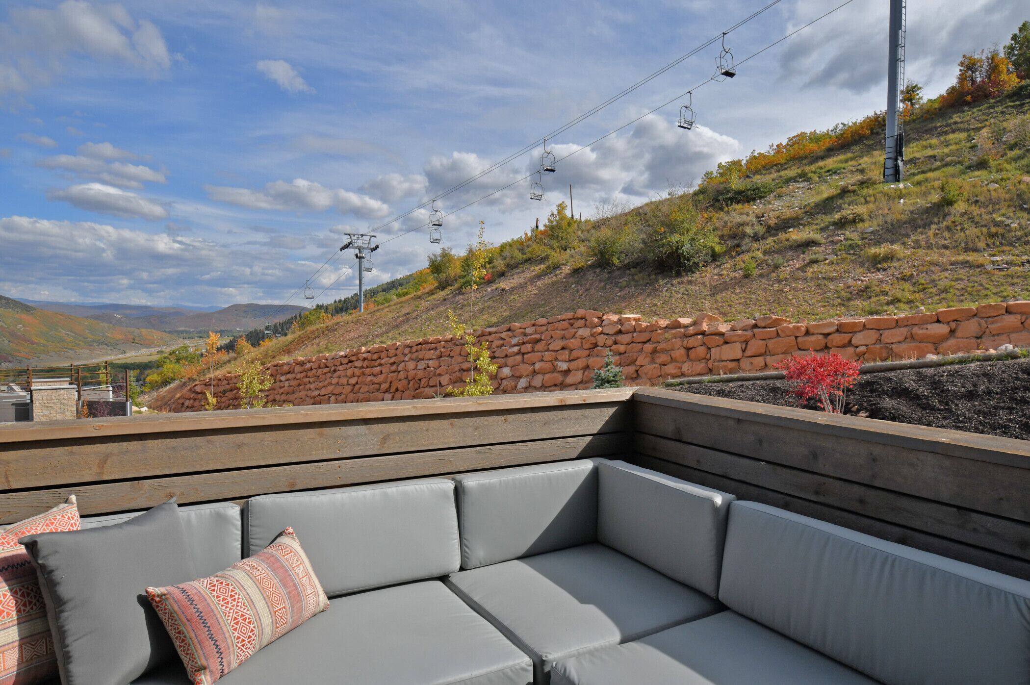 A terrace with a stone wall, a wooden bench, and a grey sofa with patterned cushions.