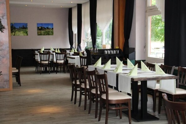 A restaurant with wooden tables and chairs, a bar area, and large windows with curtains. - Hotel Gasthof zum Ritter (Hassmersheim)