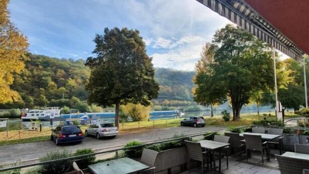 An outdoor patio with tables and chairs, overlooking a road with cars and a body of water in the background. - Hotel Gasthof zum Ritter (Hassmersheim)