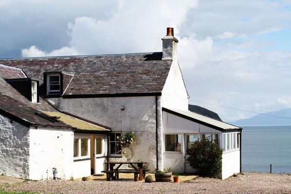 Une maison située sur la côte, dotée d’une grande fenêtre, d’une cheminée et offrant une vue sur la mer.