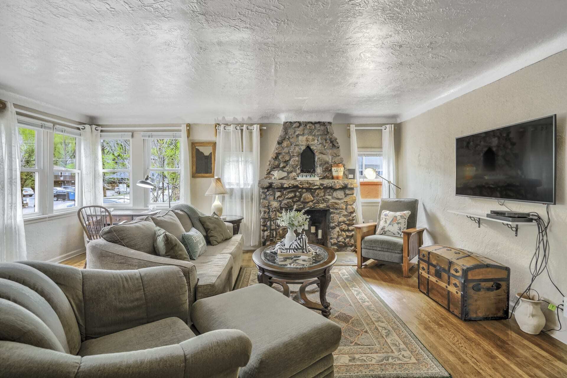 A living room with a stone fireplace, a sofa set, a television, and a vintage trunk.