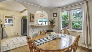 Un comedor con una mesa y sillas de madera, una cocina al fondo y una ventana con cortinas.