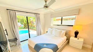 A bedroom with a bed, a nightstand, a lamp, a ceiling fan, and a view of a swimming pool. - Casinha de Alegria! - Private, Quiet Pool House (Wilton Manors)