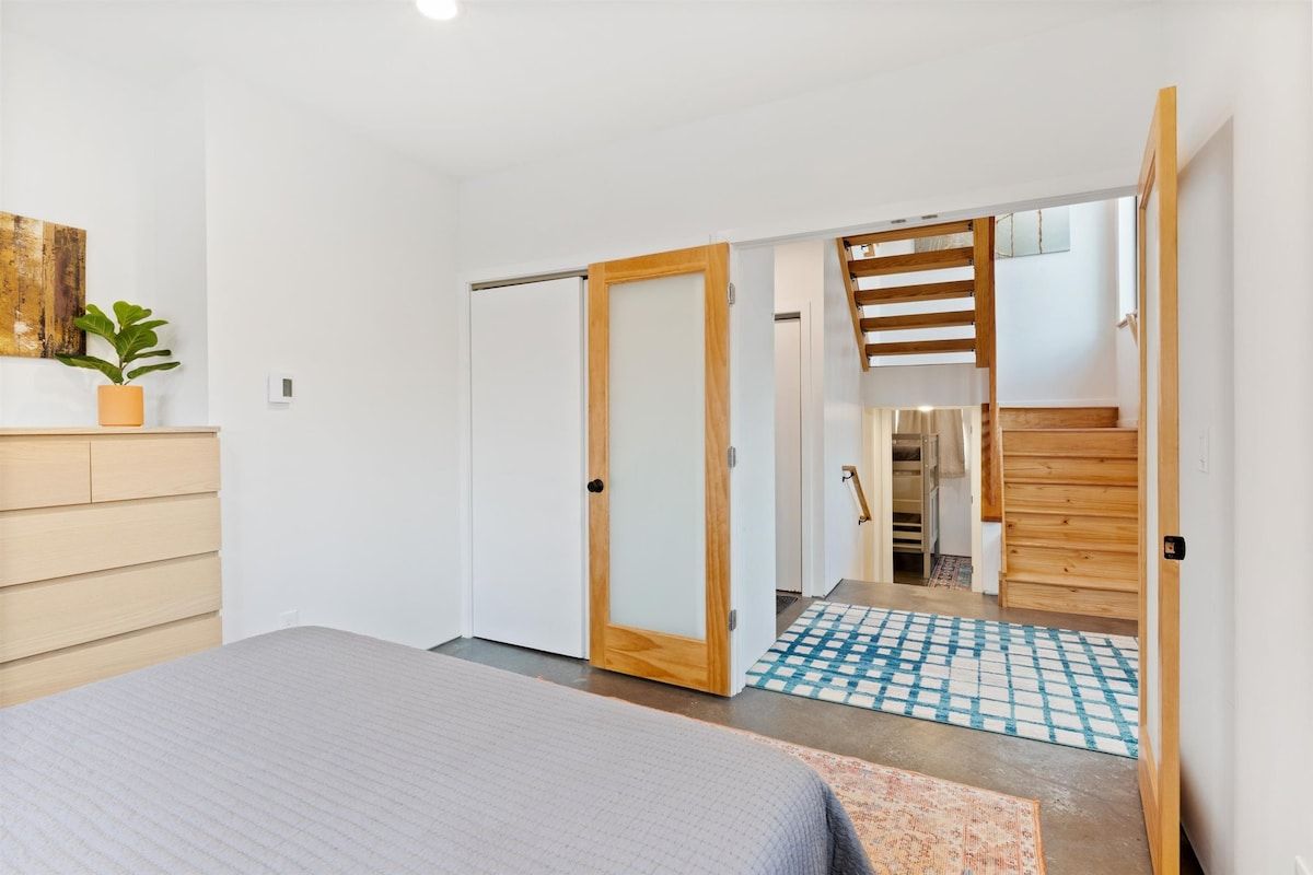 Ein Schlafzimmer mit einem Bett, einem Holzschrank, einer Tür und einer Treppe, die in einen anderen Raum führt.