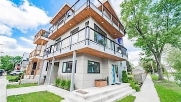 A modern two-story residential building with a balcony, a small front porch, and a well-maintained lawn.