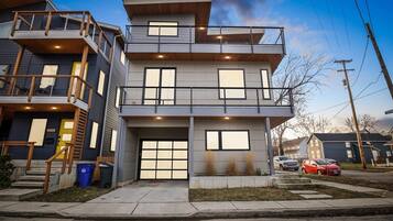 A multi-story residential building with a garage, a balcony on the second floor, and a visible driveway.