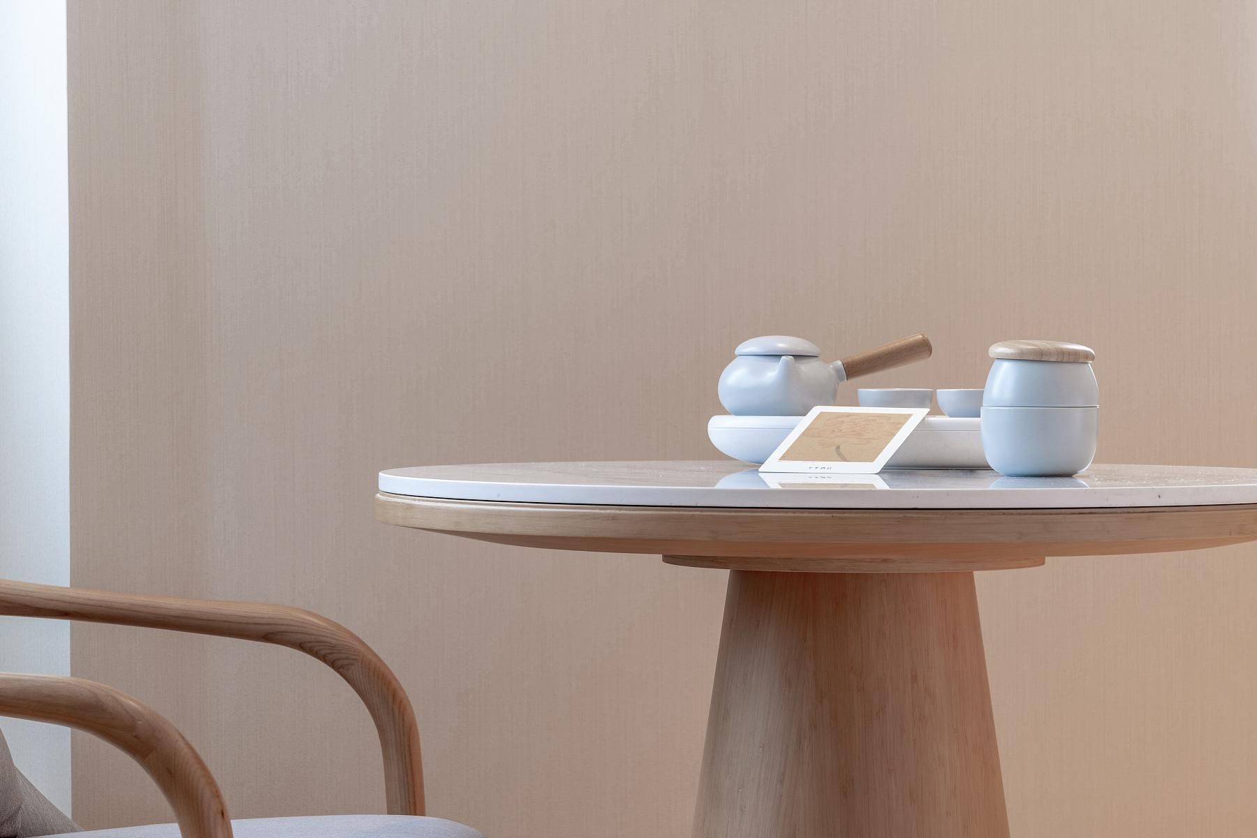 Een ronde houten tafel met een witte tafelkleed, een theepot, kopjes en een kaartje erop.