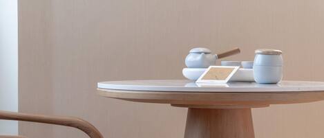 Une table ronde en bois, recouverte d’un plateau blanc, avec une théière, des tasses et une carte posées dessus.
