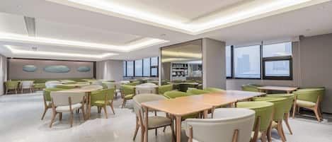 Una sala de conferencias moderna con mesas y sillas redondas, ventanas amplias y vista a la ciudad.