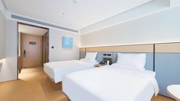 A hotel room with two beds, a bedside table with a phone and a lamp, a door with a sign, and a small wall-mounted artwork.