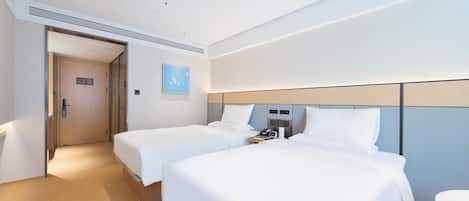 Ein Hotelzimmer mit zwei Betten, einem Nachttisch mit Telefon und Lampe, einer Tür mit einem Schild und einem kleinen Wandbild.