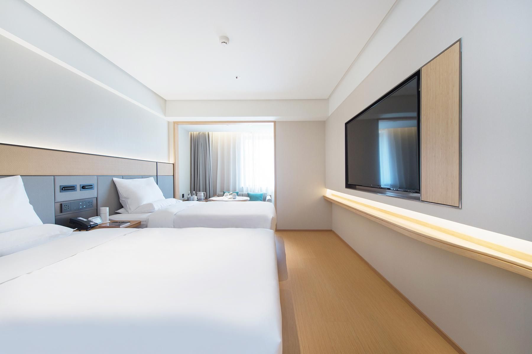 A hotel room with two beds, a TV, a desk with a phone, and a window with curtains.