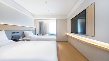 A hotel room with two beds, a TV, a desk with a phone, and a window with curtains.