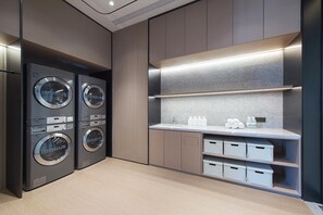 A modern laundry room with stacked washers and dryers, a sink, and storage bins. - Ji Hotel (Dalian)