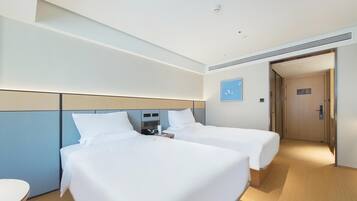 A hotel room with two beds, a bedside table, a wall-mounted phone, and a door leading to another room.