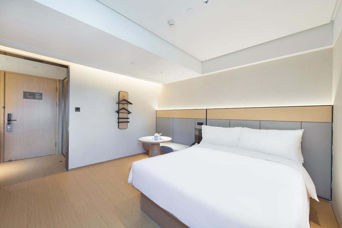 Quarto de hotel com cama, mesa de cabeceira e cabideiro.