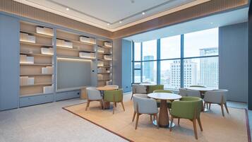 A modern library with bookshelves, round tables, and chairs, large windows with a city view.