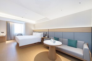 A hotel room with a bed, a sofa, a round table, and a desk with a lamp and phone. - Ji Hotel (Dalian)
