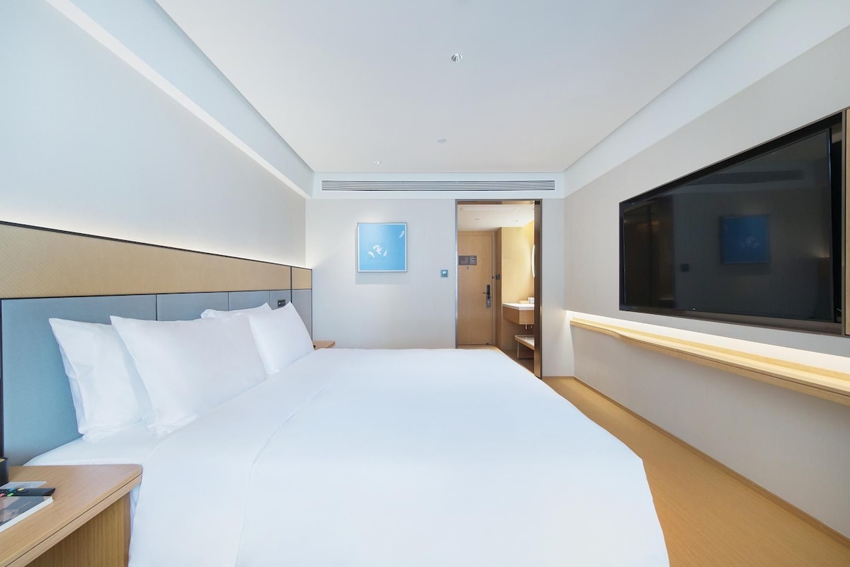 Quarto de hotel com uma cama grande, uma mesinha de cabeceira, uma televisão e uma porta para o banheiro.