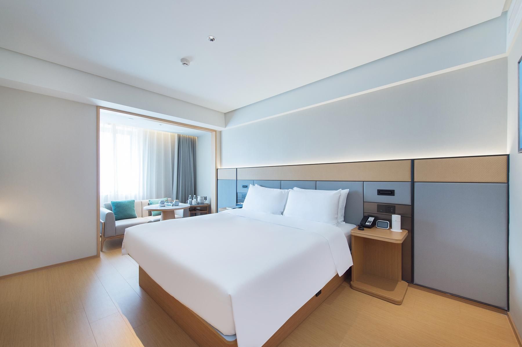 A modern hotel room with a large bed, bedside tables, a desk, and a view of the outdoors.