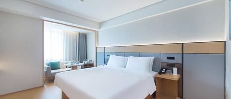 A modern hotel room with a large bed, bedside tables, a desk, and a view of the outdoors.