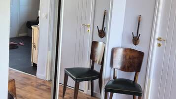 Une pièce avec un plancher en bois, un fauteuil recouvert d’un tissu vert, une chaise en bois, une porte blanche et un miroir qui reflète la pièce.
