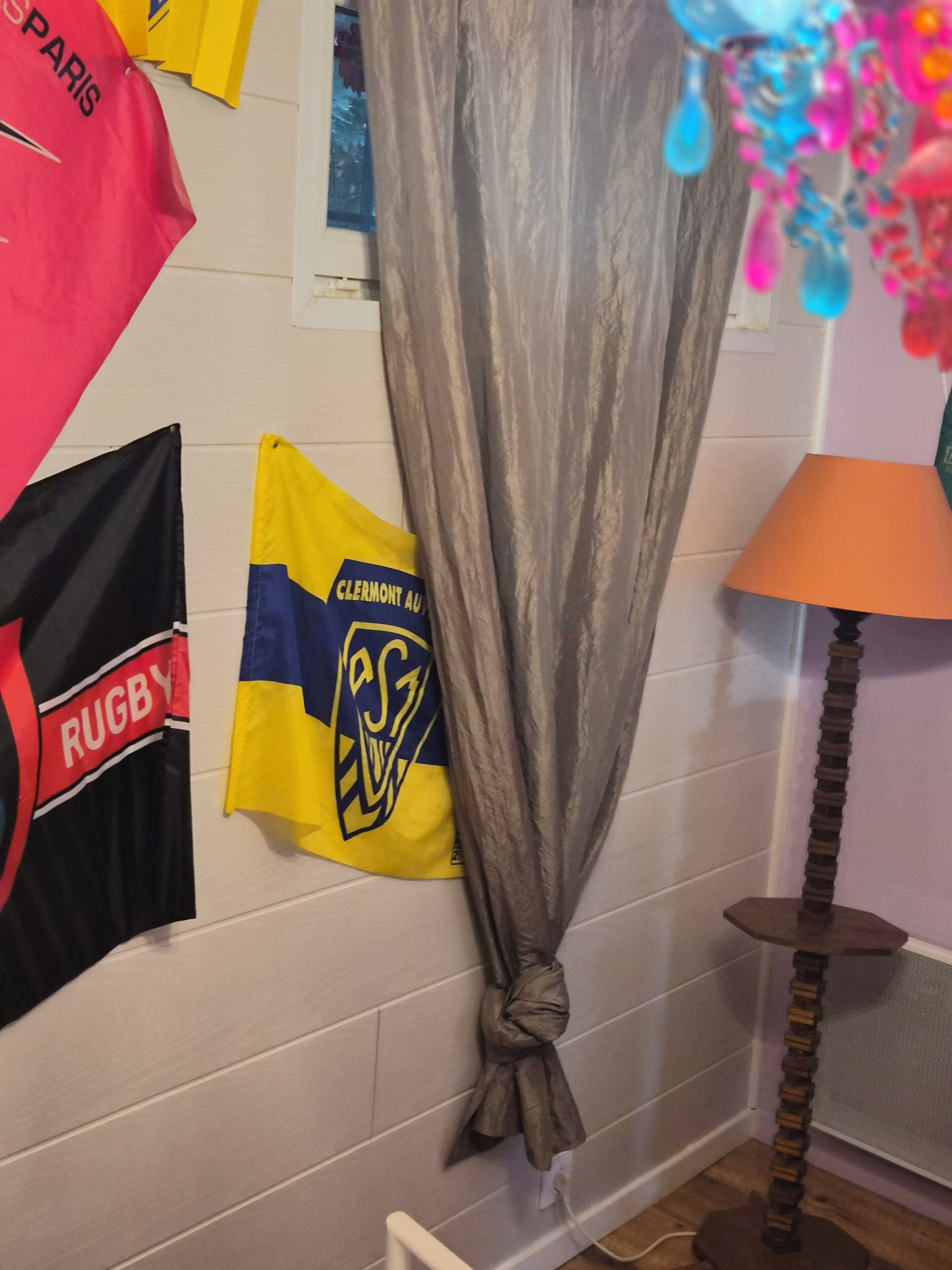Une pièce avec un drapeau de rugby, un rideau, une lampe et une étagère fixée au mur.