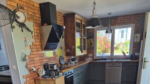 A modern kitchen with a brick wall, wooden cabinets, a glass dining table, and red chairs.