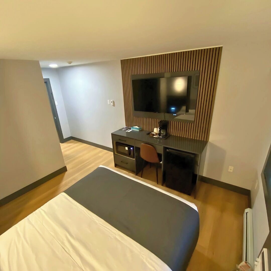 Une chambre d’hôtel comprenant un lit, un bureau avec une chaise, une télévision et une petite kitchenette.
