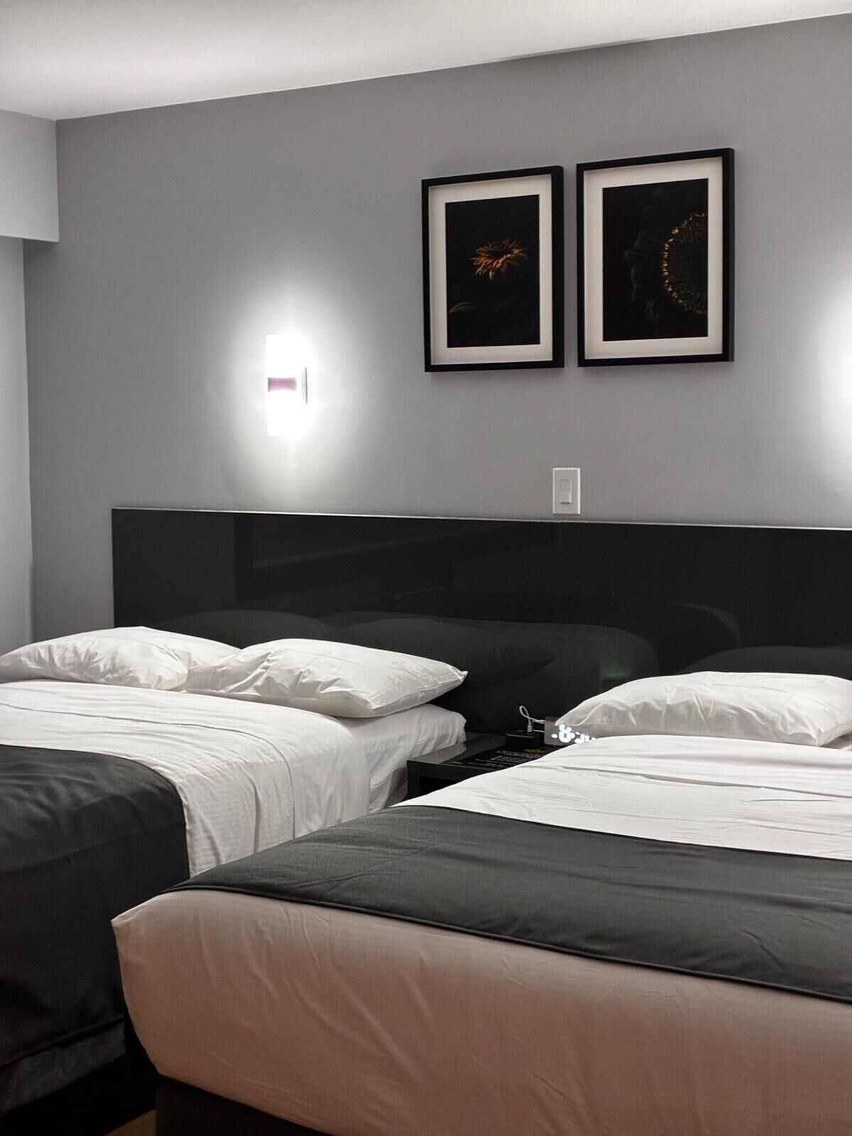 Quarto de hotel moderno com duas camas, uma televisão de tela grande e duas obras de arte emolduradas na parede.