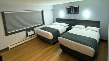 A modern hotel room with two beds, a large window, and a flat-screen TV mounted on the wall.