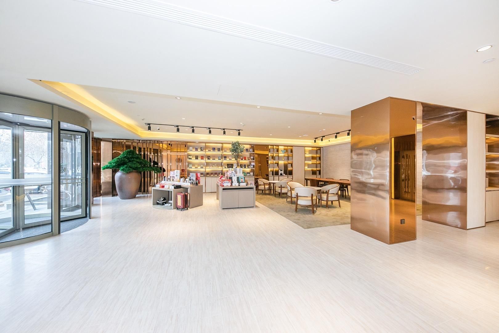 A modern hotel lobby with a central reception desk, seating area, and a large potted plant.